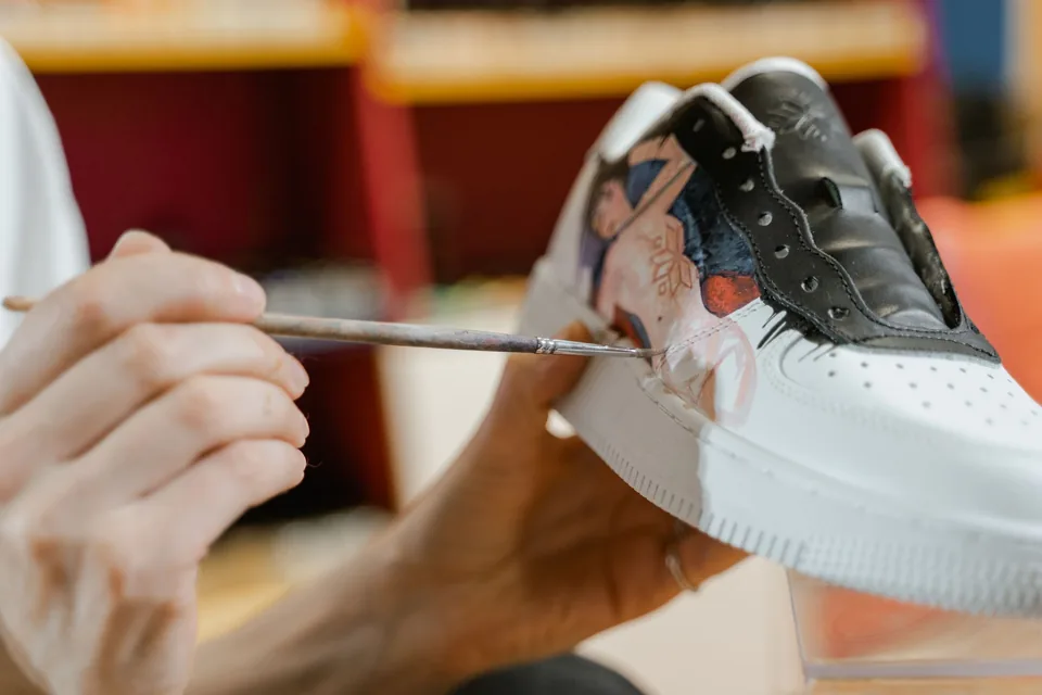 Paire de Stan Smith personnalisée à la main, posée sur un établi avec peintures et pinceaux.